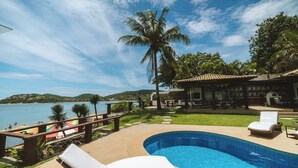 Una piscina con sillones de descanso, una palmera y vistas al mar.
