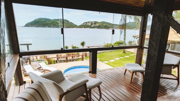 Una terraza de madera con un sofá y sillas, con vista a una piscina y un paisaje pintoresco de un lago y colinas.