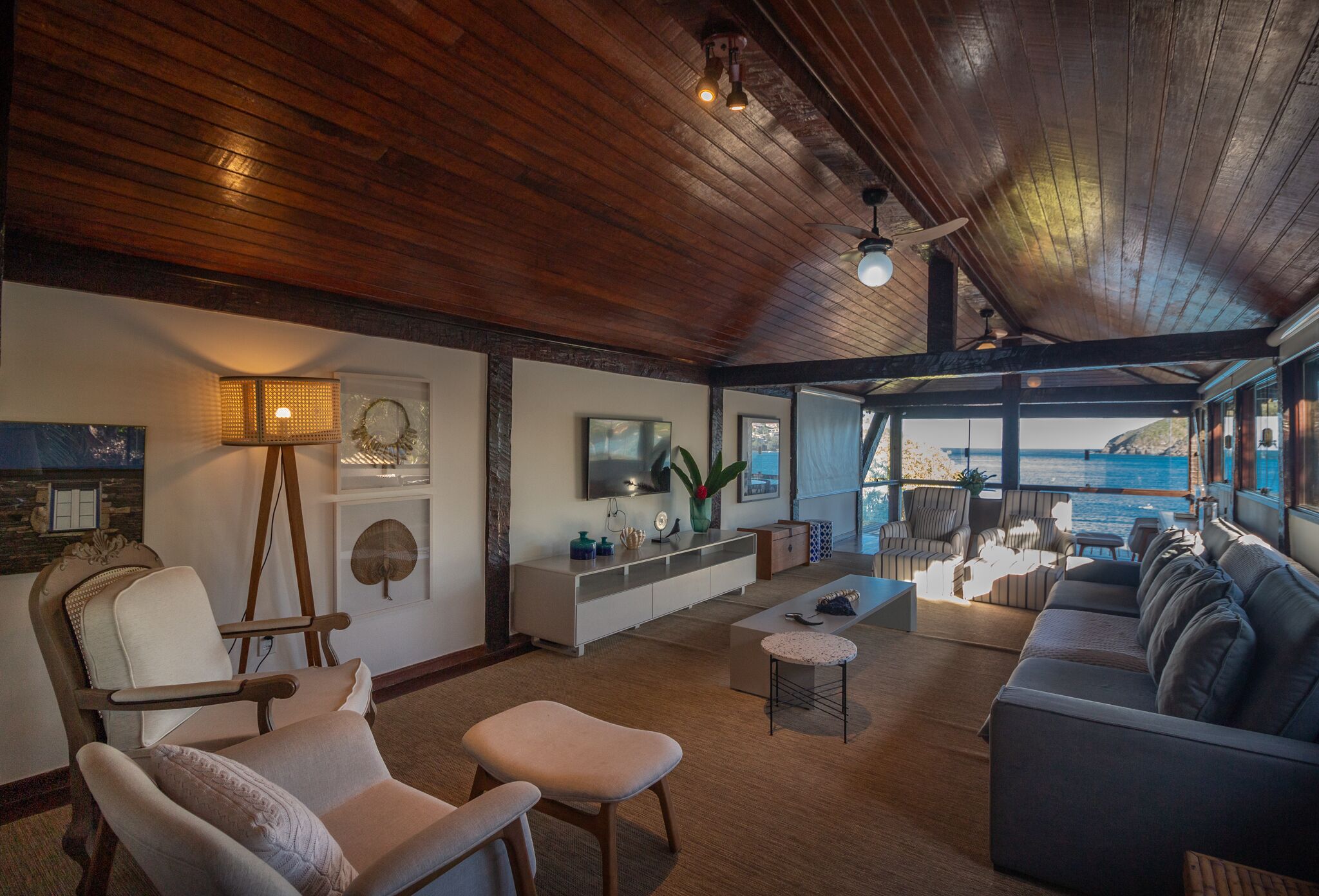 A spacious living area with a wooden ceiling, a large sofa, a coffee table, and a view of the ocean.