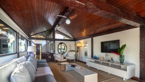Un salón amplio con techo alto, un sofá grande, una mesa de centro, un televisor y un mueble de entretenimiento blanco.