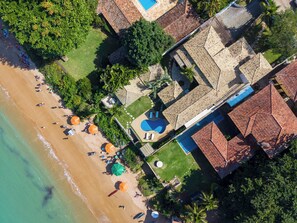 Vista aérea de un resort con playa, piscina y varias edificaciones con techos de tejas rojas.
