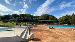 Un espace piscine avec un sol carrelé, des chaises longues et un bâtiment en arrière-plan.