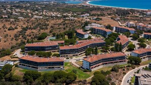 Vue aérienne d’une zone résidentielle côtière, avec des immeubles d’appartements modernes, une plage et un ciel bleu dégagé.