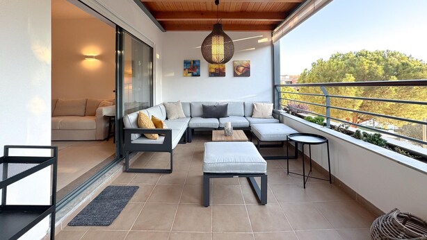 Un balcon moderne avec un plafond en bois, un ensemble de canapés gris, une petite table et un luminaire suspendu.