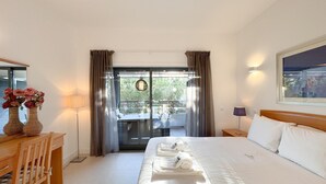 Une chambre d’hôtel comprenant un lit, un bureau avec une chaise, un vase de fleurs, un balcon avec une table et des chaises, et une vue sur l’extérieur.