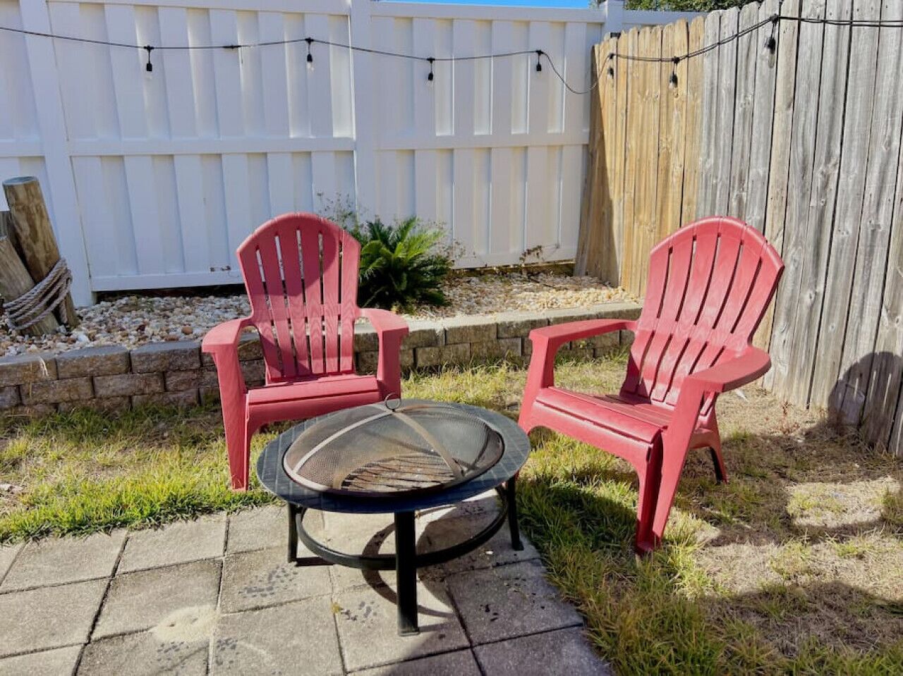 Un espace patio aménagé avec deux chaises Adirondack rouges et une table ronde dotée d’un gril en métal.