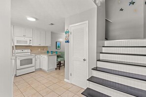 Una cocina con armarios blancos, un microondas y un horno. Hay una pequeña isla con una silla y un cuadro en la pared.