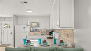 A compact kitchen with white cabinets, a refrigerator, a sink, and a dining area with a table set for two.