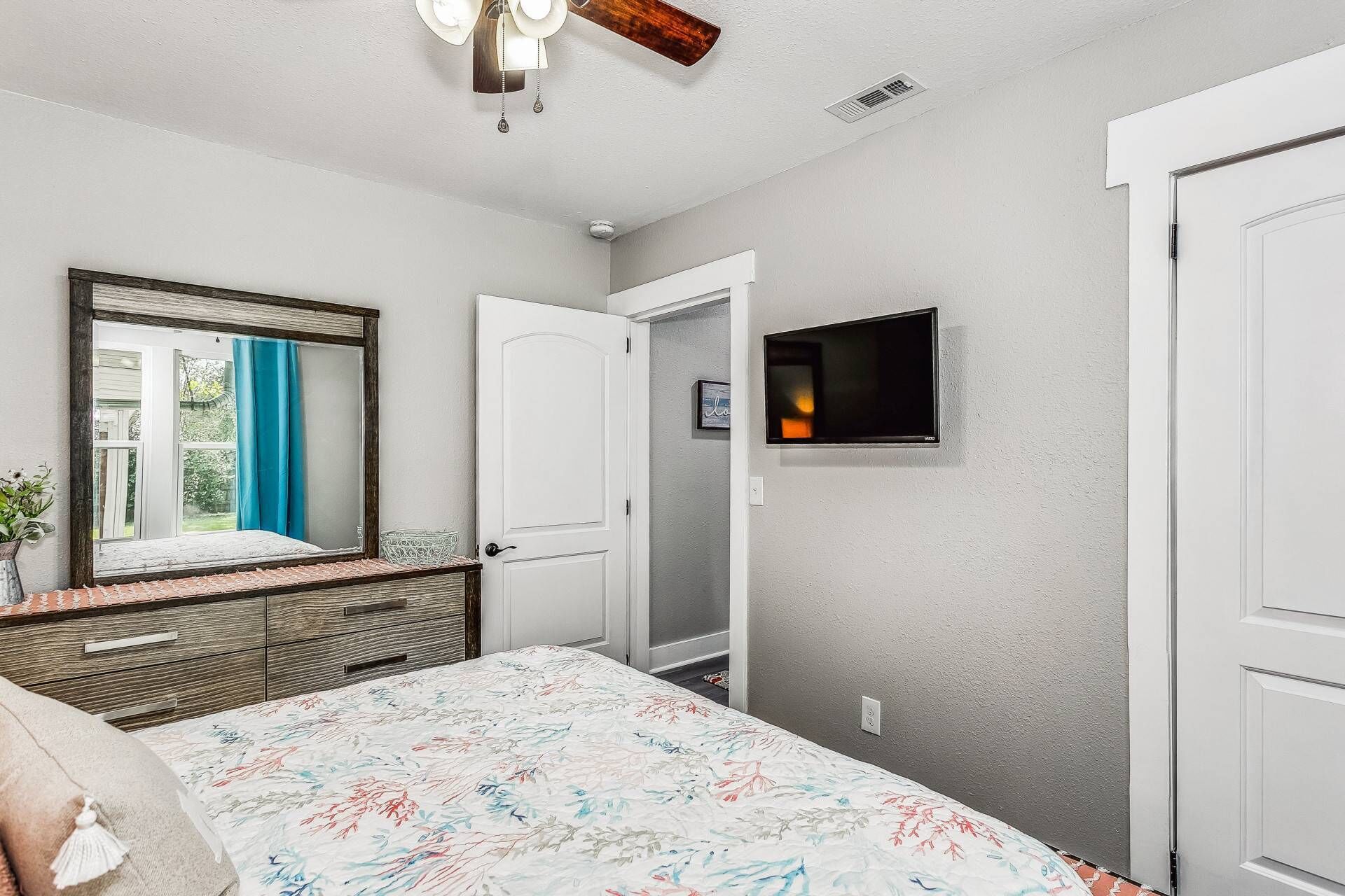 A bedroom with a bed, a dresser, a mirror, a door, and a TV mounted on the wall.