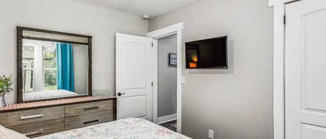 A bedroom with a bed, a dresser, a mirror, a door, and a TV mounted on the wall.