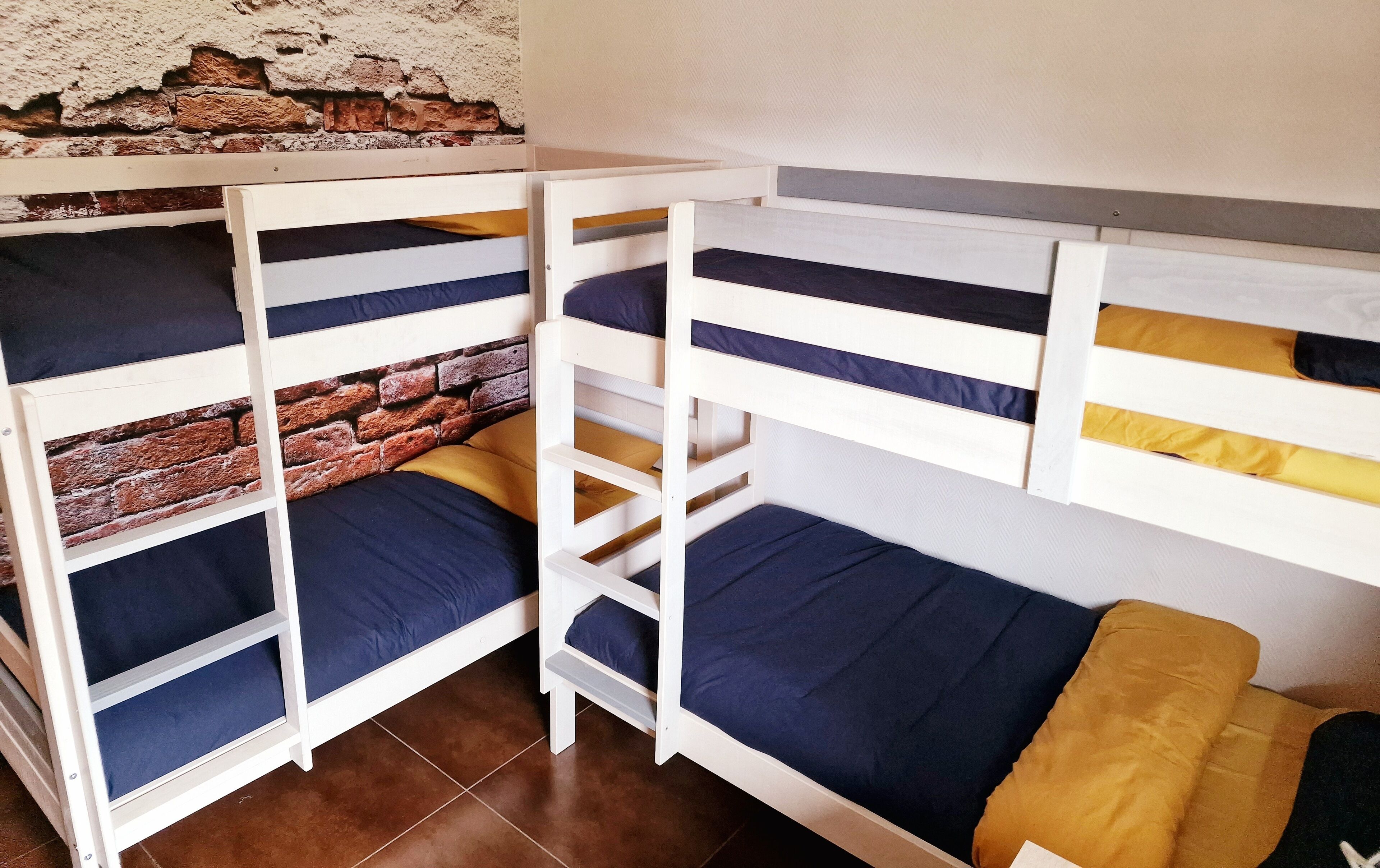 Una habitación con literas, una pared de ladrillo y suelo de baldosas.