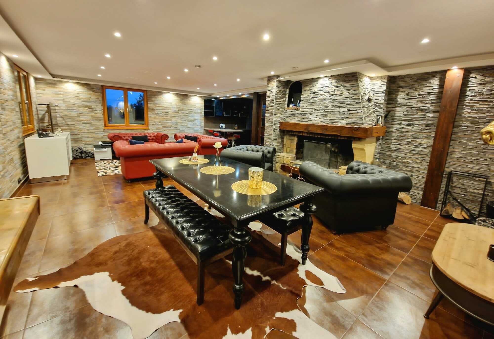 Una sala de estar moderna con chimenea de piedra, sofás de cuero, una mesa de comedor y un alfombrado de piel de vaca.