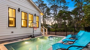 Una piscina con un canestro da basket, poltroncine blu e un edificio bianco con finestre.