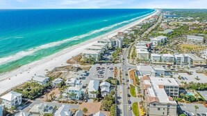 Una vista aerea di una cittadina costiera con spiaggia, edifici residenziali e cielo sereno.