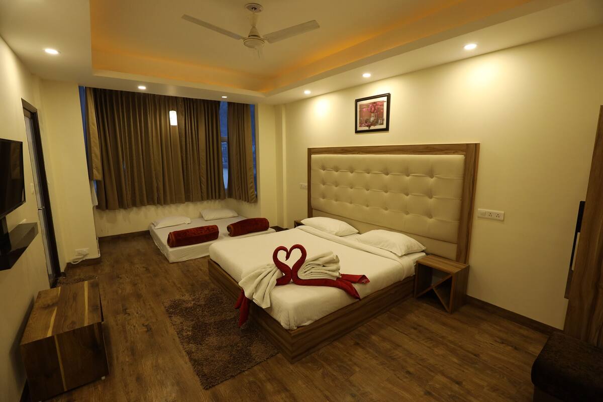 A hotel room with a large bed, a sofa, a TV, and a ceiling fan.