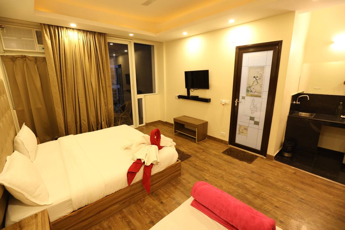 A hotel room with a bed, a TV mounted on the wall, a small desk, and a door with a window.