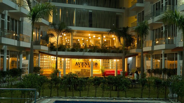 Un hotel de diverses plantes amb zona de piscina, amb balcons decorats amb plantes i una entrada ben il·luminada.
