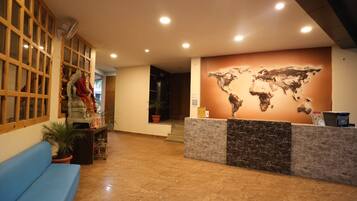 Zona de recepció amb taulell de marbre, un sofà blau, un mural d'un mapa mundial i una separació de fusta amb cortines decoratives.