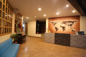 A reception area with a marble reception desk, a blue sofa, a world map mural, and a wooden partition with decorative curtains. - Avenue 18 Resort (Yamkeshwar)