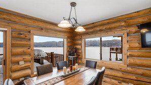 Een houten chalet van binnen, met een eettafel gedekt voor zes personen, een kroonluchter en uitzicht op een meer en bergen door grote ramen.