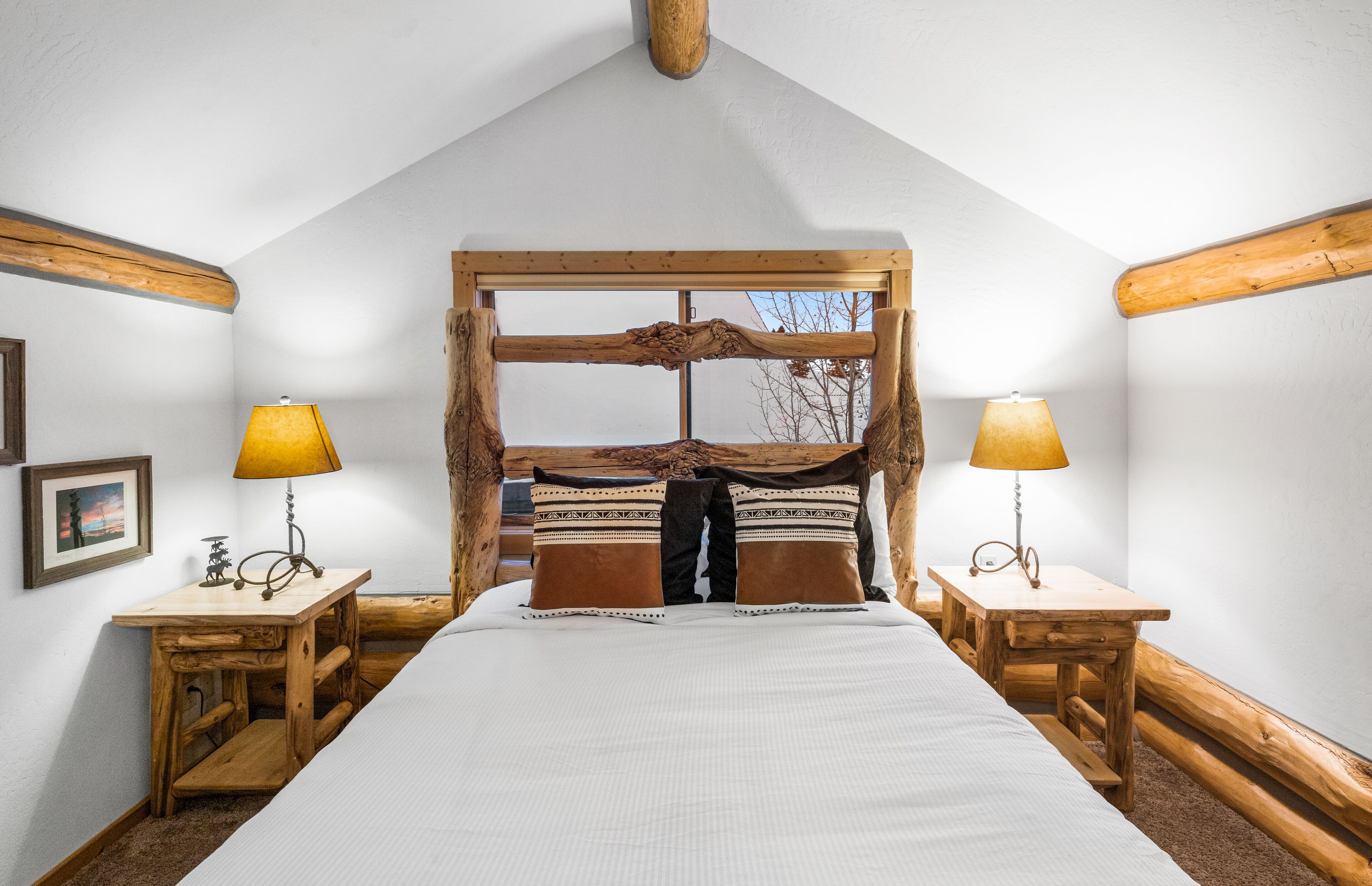 A bedroom with a large bed, wooden headboard, two bedside tables with lamps, and a framed picture on the wall.