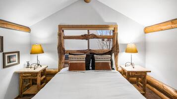 A bedroom with a large bed, wooden headboard, two bedside tables with lamps, and a framed picture on the wall.