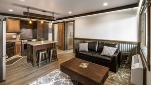 Un vaste espace de vie comprenant un canapé en cuir, une table basse et un coin cuisine avec des meubles en bois et un mur de fond en briques.