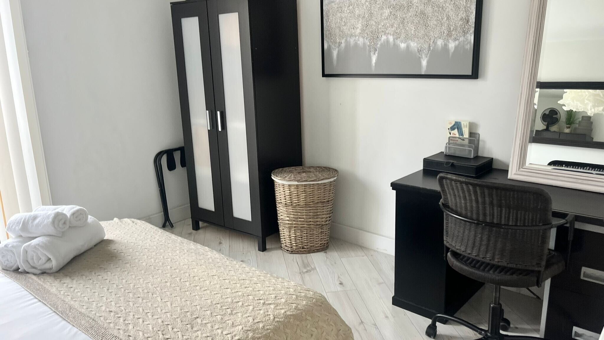 A bedroom with a bed, a desk, a chair, a wicker basket, and a framed picture on the wall.