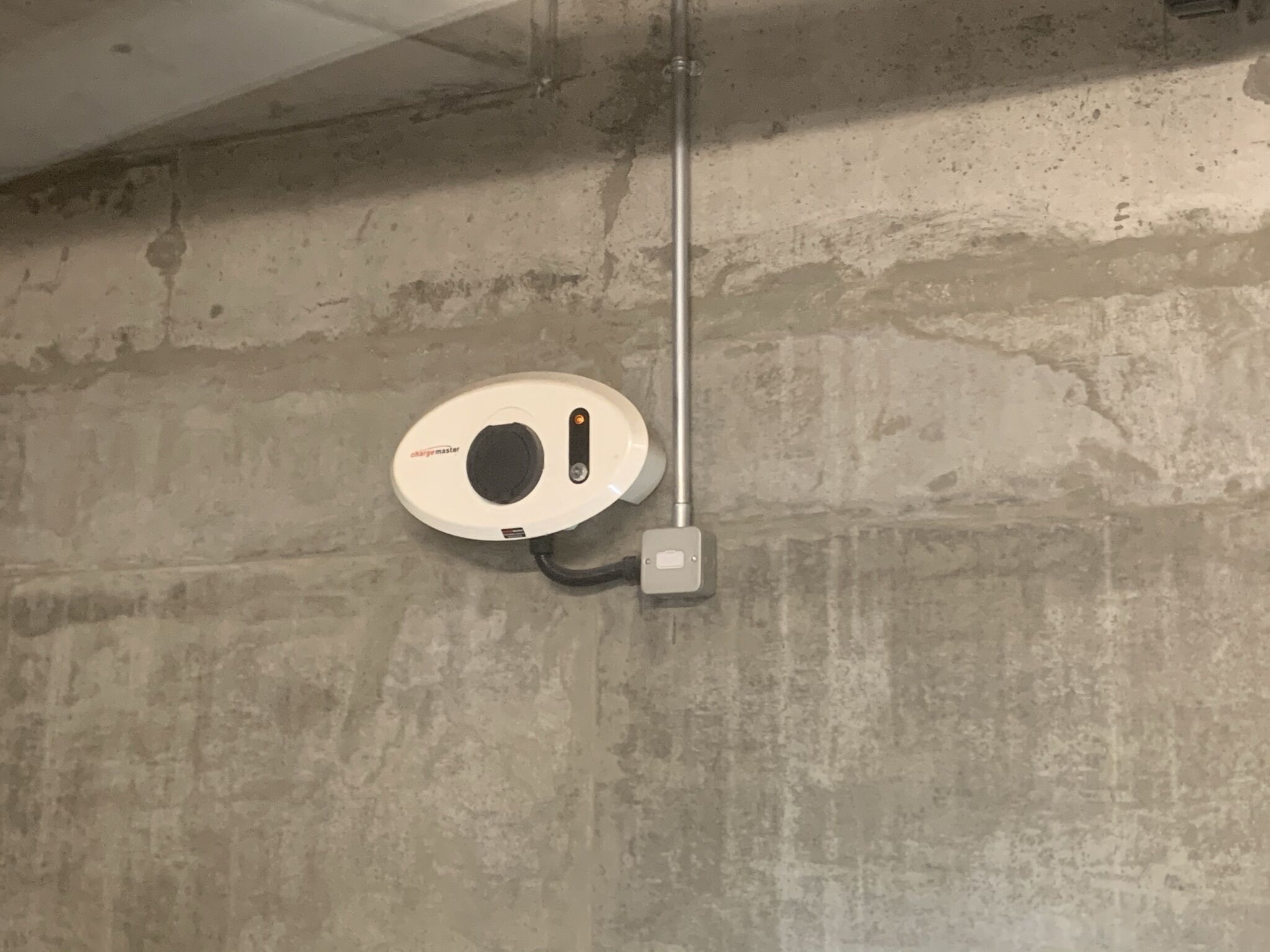 A ceiling-mounted smoke detector on a textured concrete wall.