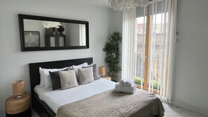 A bedroom with a large bed, a mirror, a potted plant, and a view of the outside through a sliding door. - Notting Hill 2-bed Apt With Balcony, 1 min to Tube (London)