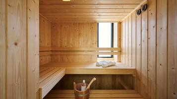 Una sauna de madera con bancos, una ventana, un balde con una toalla y una botella.