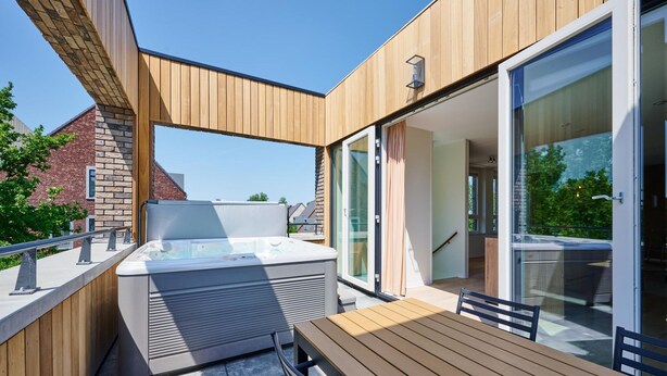 A modern outdoor patio with a hot tub, wooden deck, and glass doors leading to an interior space. - Maastricht Wellness Loft (Maastricht)