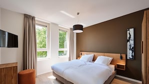 A modern bedroom with a large bed, a TV mounted on the wall, and a window with curtains. - Maastricht Wellness Loft (Maastricht)