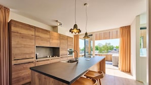 A modern kitchen with wooden cabinets, a central island with stools, pendant lighting, and a view to the outdoors. - Maastricht Wellness Loft (Maastricht)