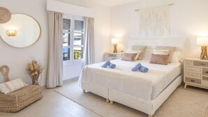 A spacious bedroom with a large bed, bedside tables, a woven chair, and a view through the window. - Puerto Banus OPQ by Interhome (Marbella)