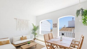 A bright, airy living room with a sofa, coffee table, and dining table. There are two windows with views of buildings and a plant hanging from the ceiling. - Puerto Banus OPQ by Interhome (Marbella)