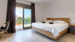 A modern bedroom with a large bed, a chair, and a sliding glass door leading to an outdoor area.