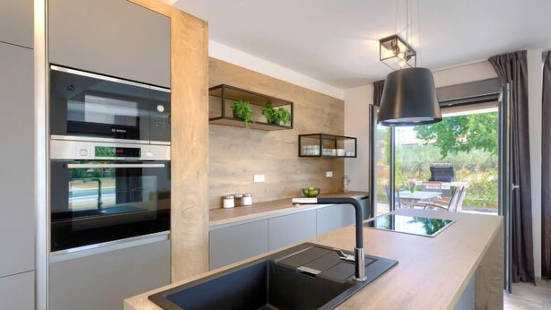 A modern kitchen with built-in appliances, a central island with a sink, and a view of the outdoors.