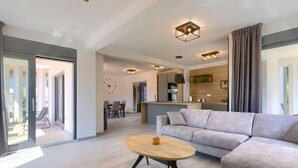 A modern living room with a sofa, a coffee table, and a dining area in the background.