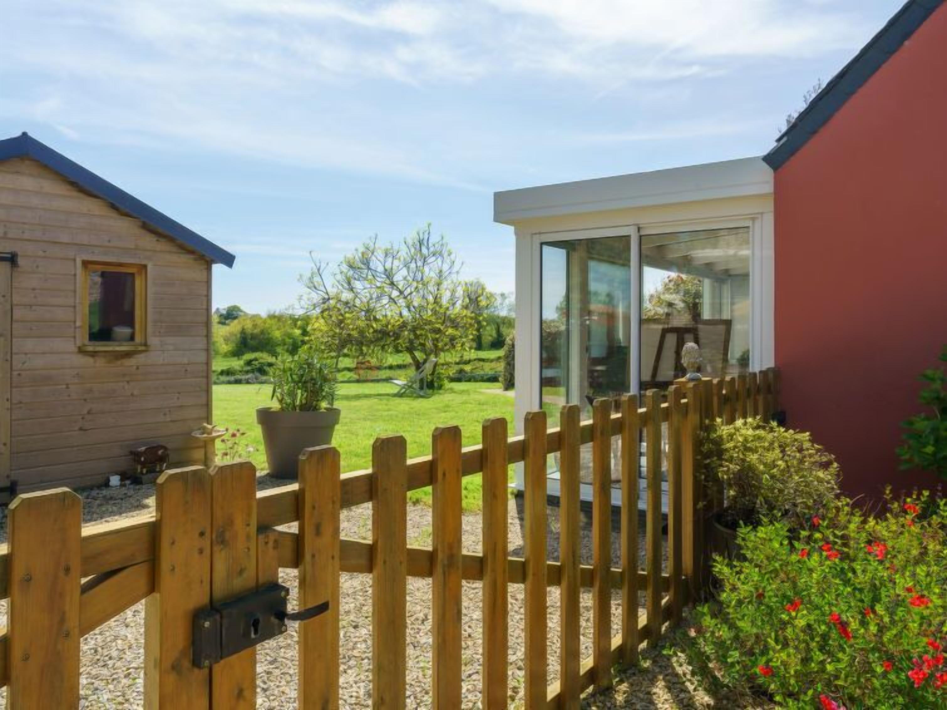 Ein Holzhaus mit einem eingezäunten Garten und einer Glastür, die zu einem Zimmer führt.