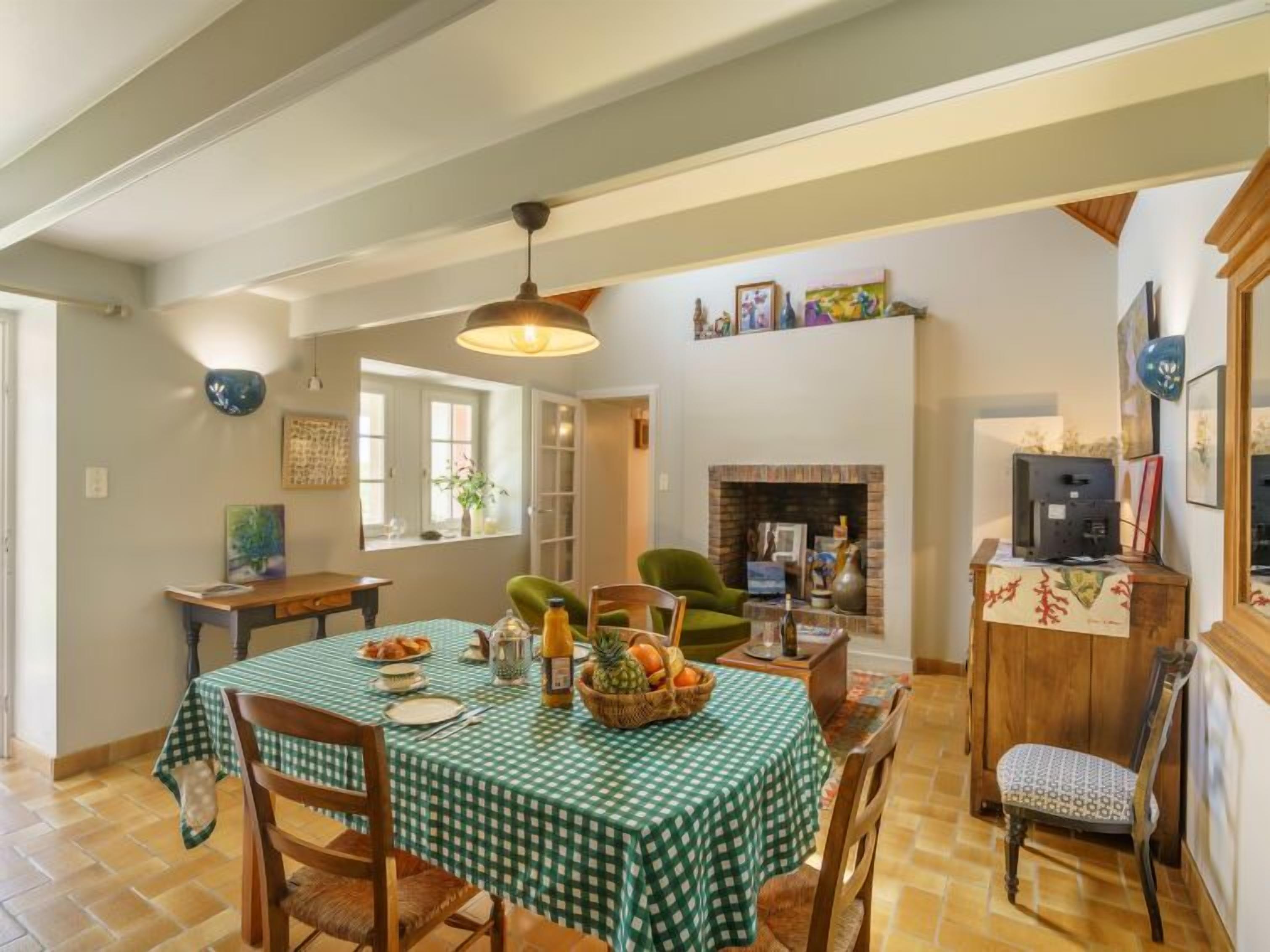 Un comedor con mantel a cuadros, sillas de madera, una lámpara colgante, chimenea y obras de arte en las paredes.