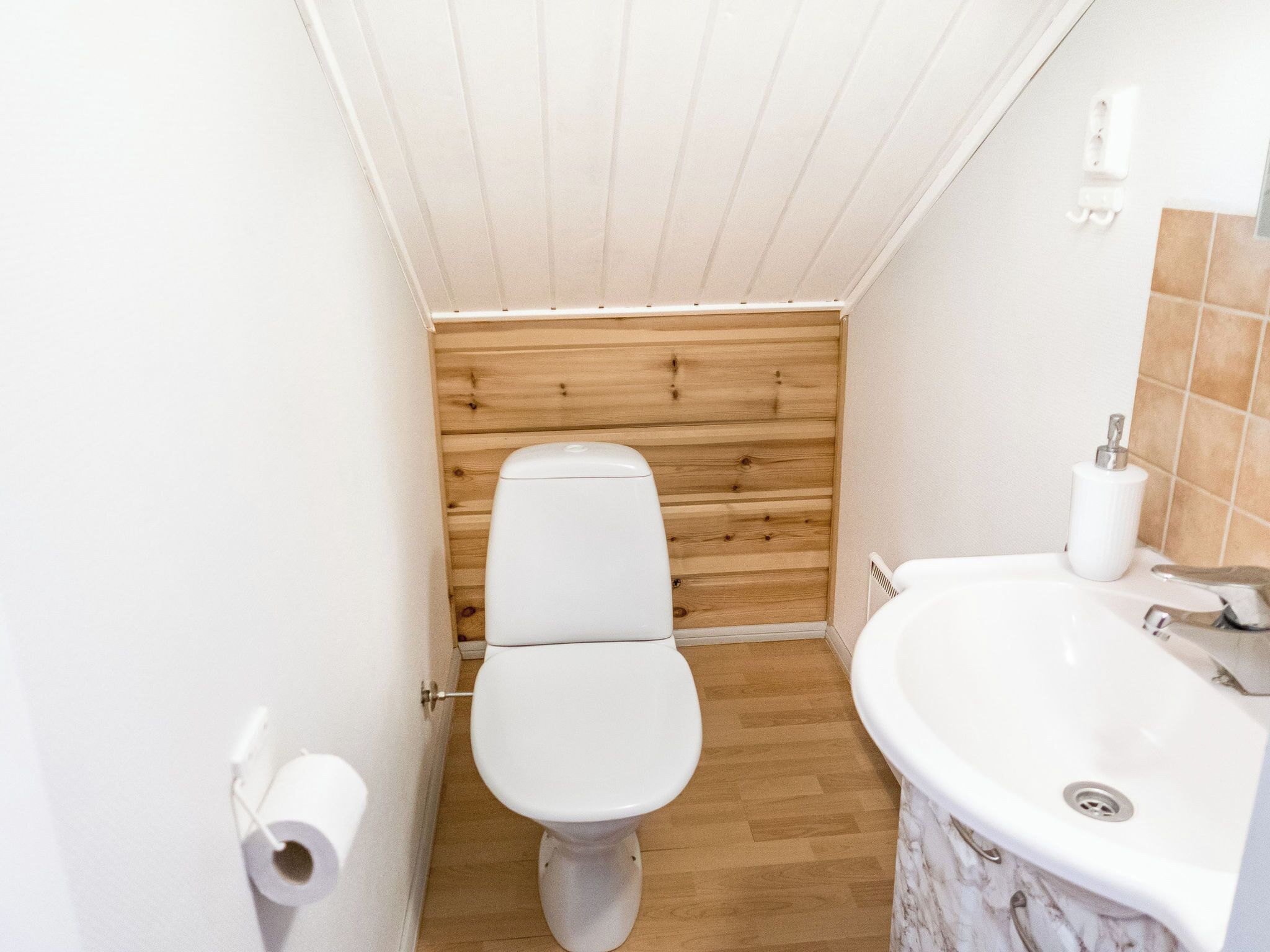 A small bathroom with a toilet, a sink, and wooden paneling on the wall.