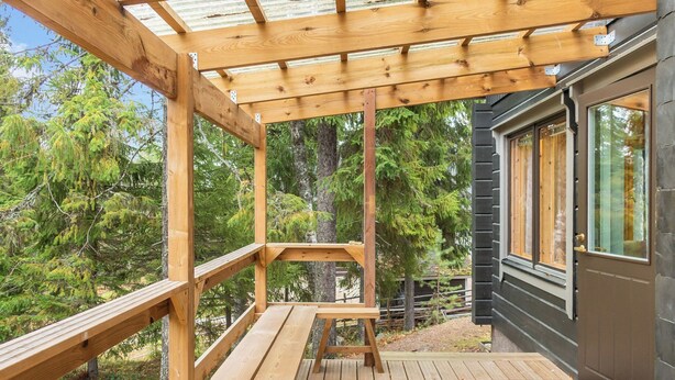 Une terrasse en bois agrémentée d’une pergola, d’un banc et offrant une vue sur une forêt.