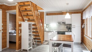 Une cuisine moderne avec des meubles blancs, un escalier en bois et un coin repas comprenant une table et des chaises en bois.
