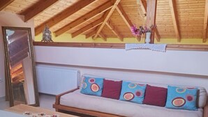 Una habitación acogedora con techo de madera, un sofá con cojines de colores, un espejo y un radiador.