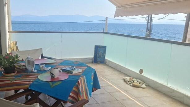 Un balcón con una mesa lista para dos personas, una planta en maceta y vista al mar.