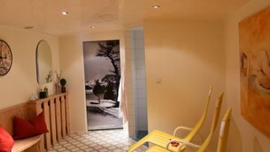 A spa room with a wooden bench, yellow chairs, a painting, and a view of a snowy landscape. - Apartment Gams by Interhome (See)