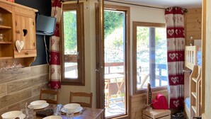 A cozy room with a wooden dining table set for four, a television mounted on the wall, and a window with a red and white heart-patterned curtain. - Renovated 16m² studio, close to slopes, Avoriaz (Avoriaz)