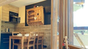 A modern kitchen with wooden cabinets, a built-in oven, and a dining area with a table and chairs. - Renovated 16m² studio, close to slopes, Avoriaz (Avoriaz)