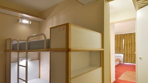 Une chambre avec un lit superposé, une échelle, une petite table et une porte donnant sur une autre pièce.